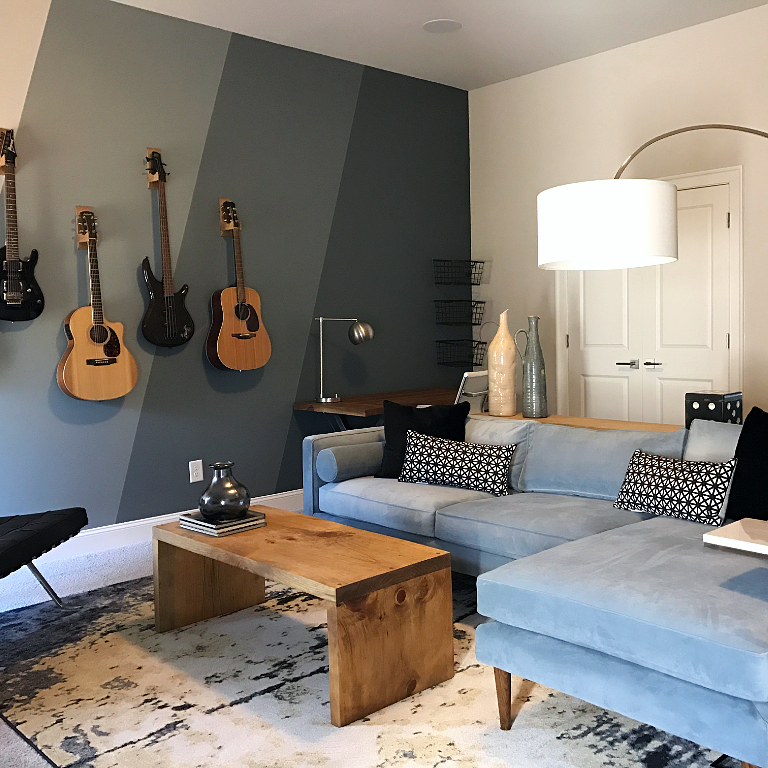 home music room with large sectional couch and guitars on the wall photo by Instagram user @houseliftdesign