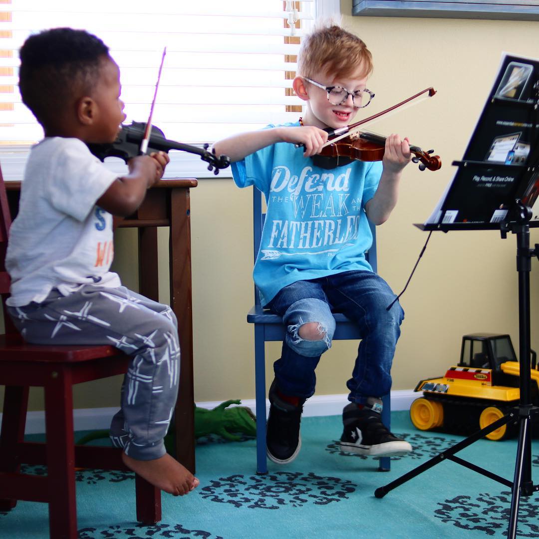 two young kids playing violins in a small music room photo by Instagram user @amymlantz