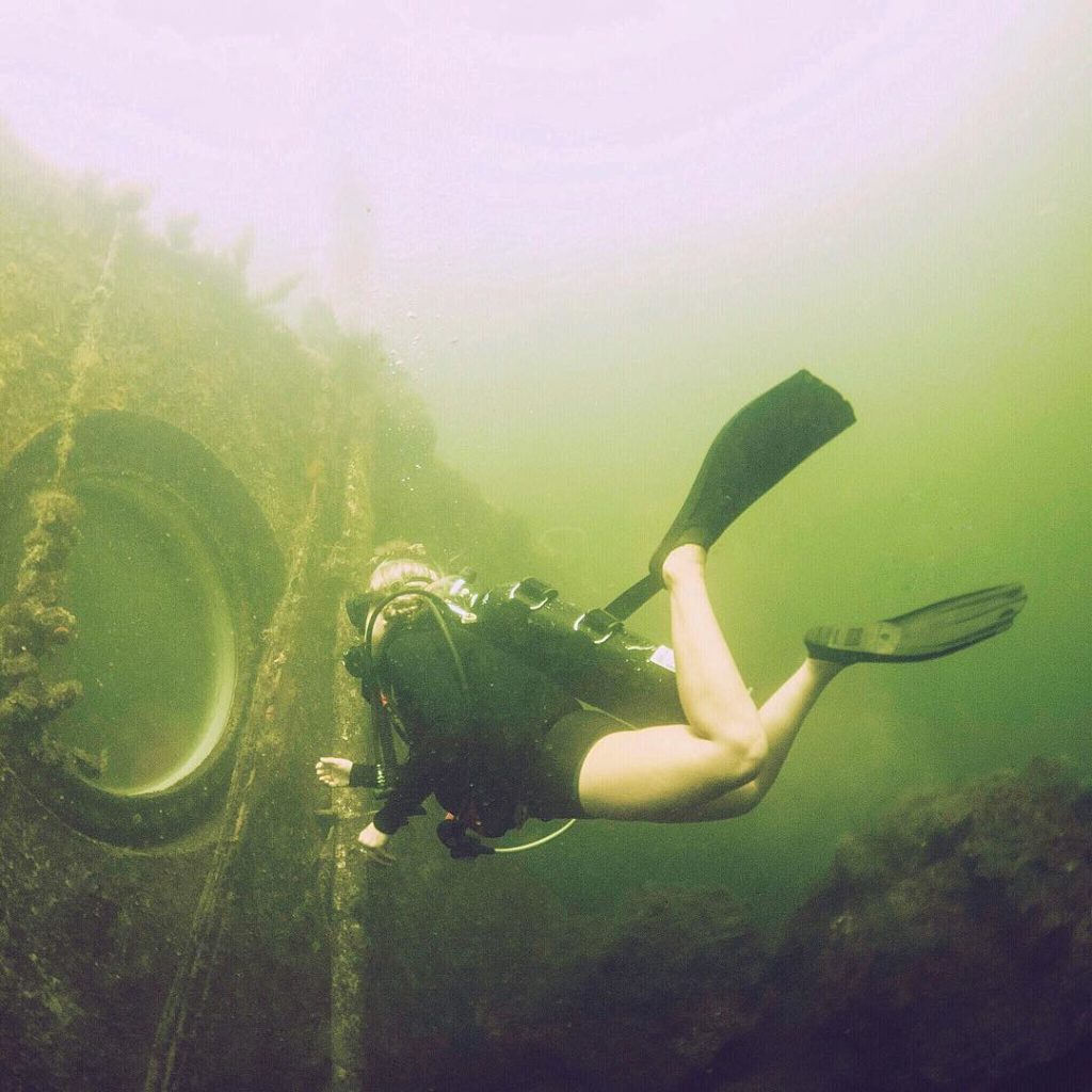 Scuba diver looking into underwater hotel room window. Photo by Instagram user @alexinwanderland