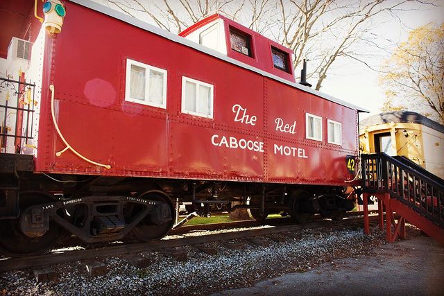 Red train caboose on train tracks in daylight. Photo by Instagram user @redcaboosemotel
