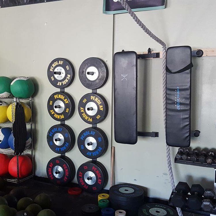 Barbell weights and benches hung from wall in gym. Photo by Instagram user @bullcitystrong