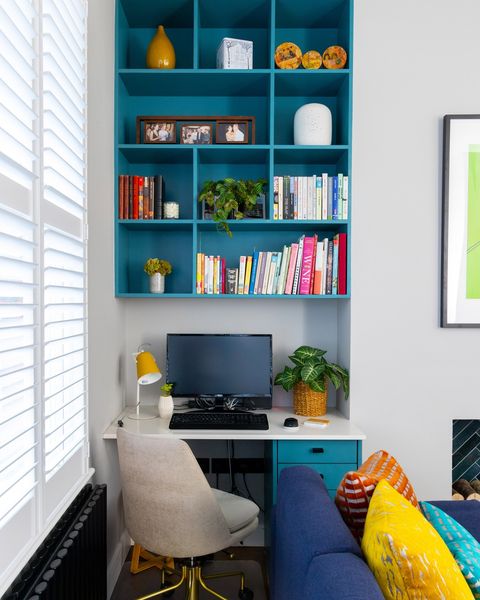 A nook of a home with blue shelving. holdings books, and other decorations, with a desk and offcie chair. @ahrbergjacksondesign