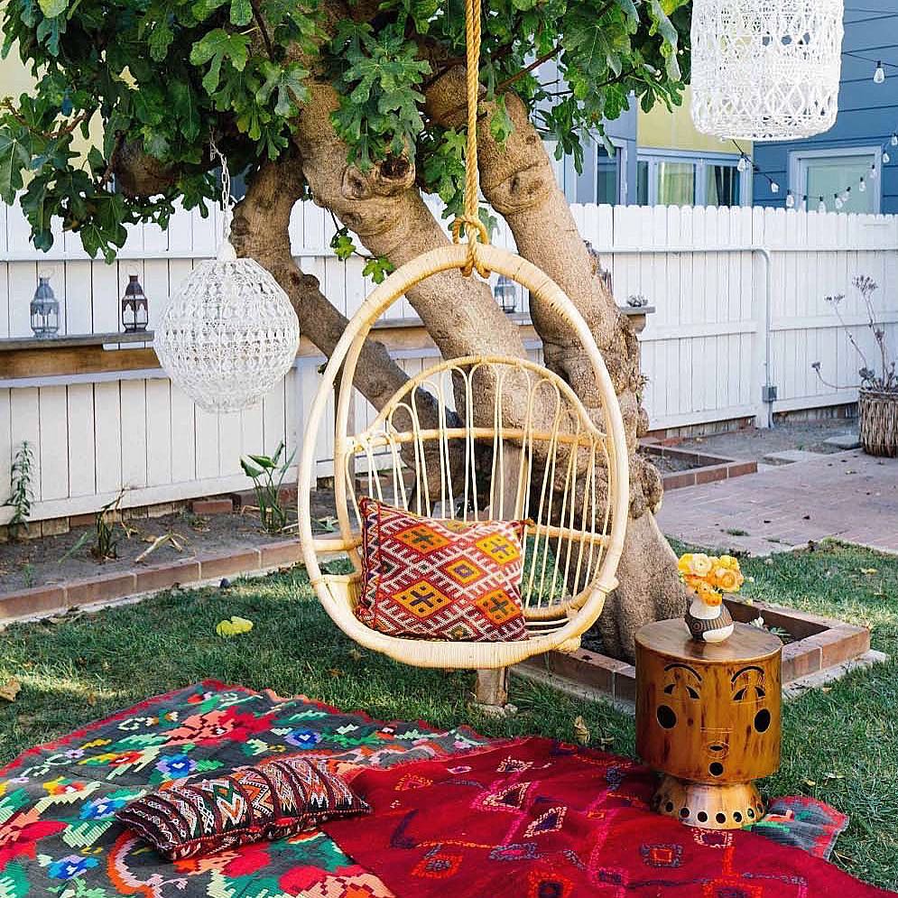 Chair hanging from tree with red rugs on ground. Photo by Instagram user @trangjanick
