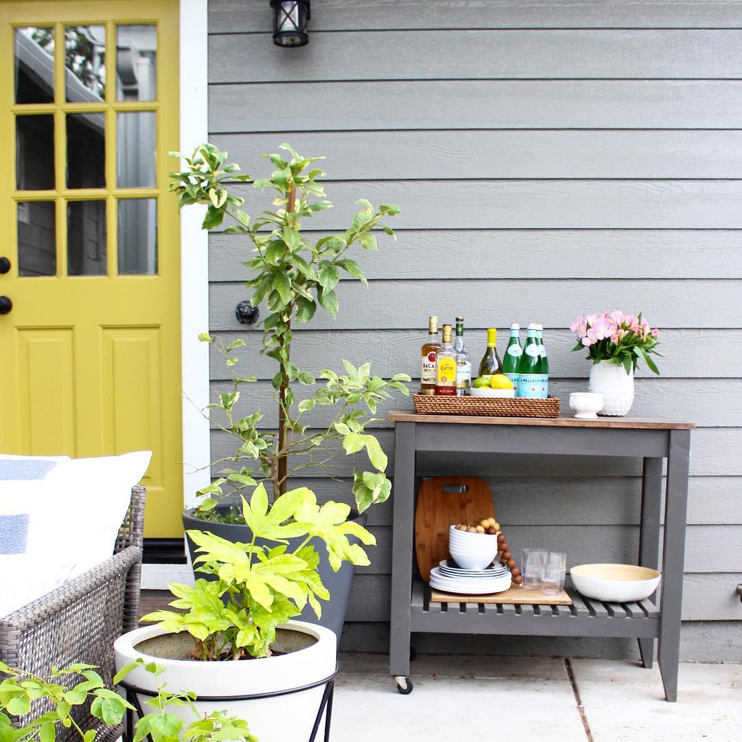 Wooden outdoor bar cart by yellow door. Photo by Instagram user @thekatrinablair