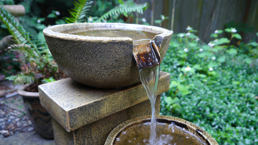 A bowl shaped water feature made of stone with a waterfall pouring into another bowl