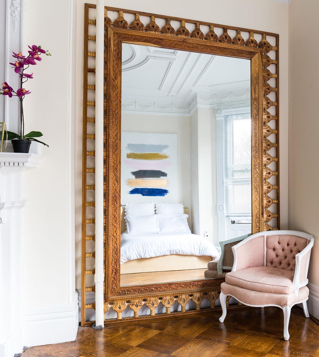 large mirror in bedroom to extend the room with pink chair next to it photo by Instagram user @apartmenttherapy