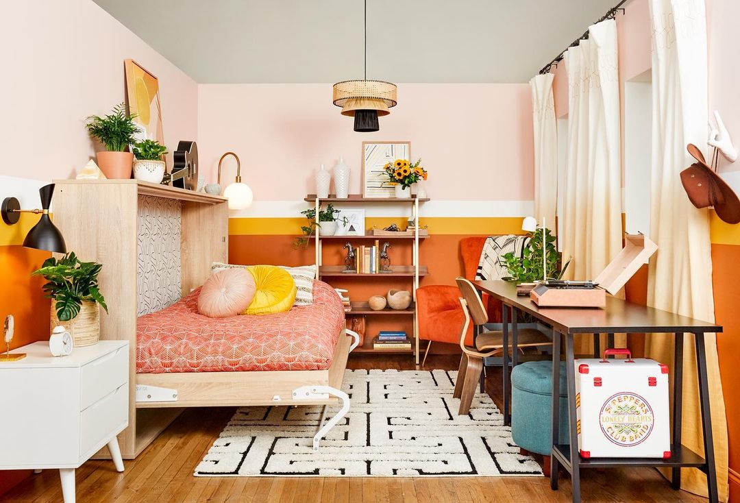 a colorful bedroom with a light wood murphy bed unfolded and the bed made with a pink comforter and yellow pillows