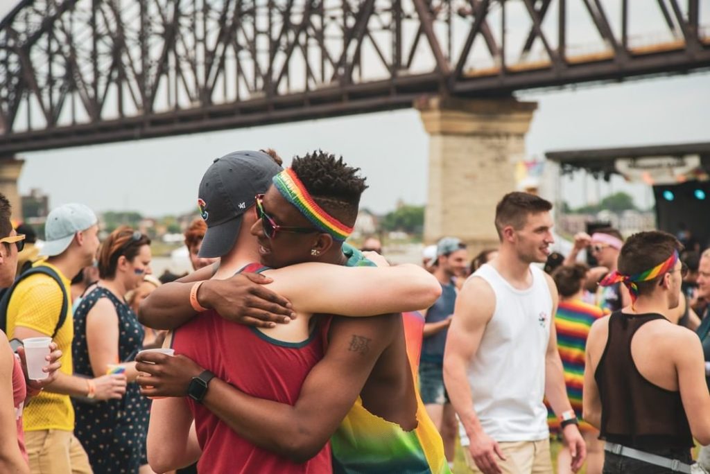 Two people in colorful tanktops embrace in front of a crowd at the Kentuckiana Pride festival.