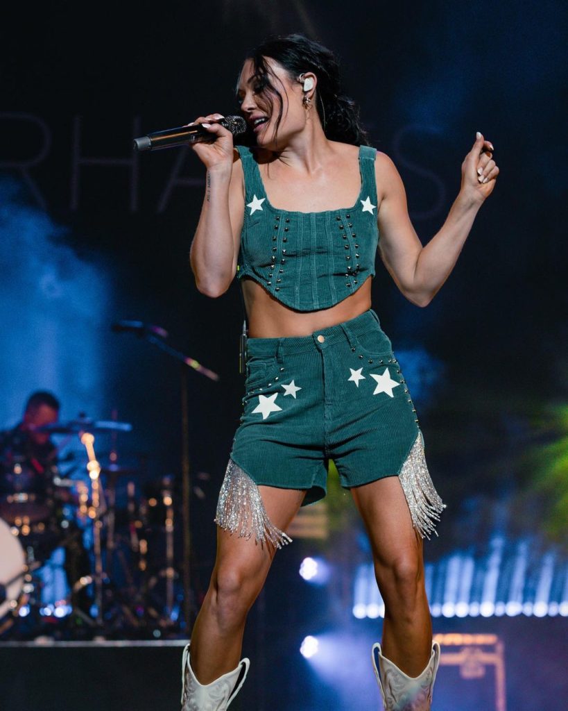 A female musician, Kylie Morgan, in two-piece dark green outfit singing on stage. 