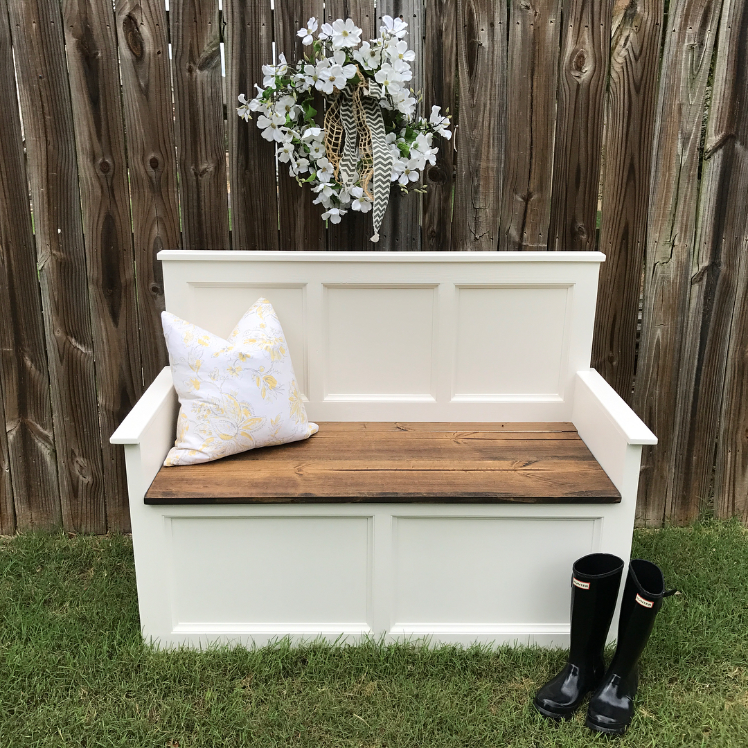 White storage bench next to fence with white flowers.