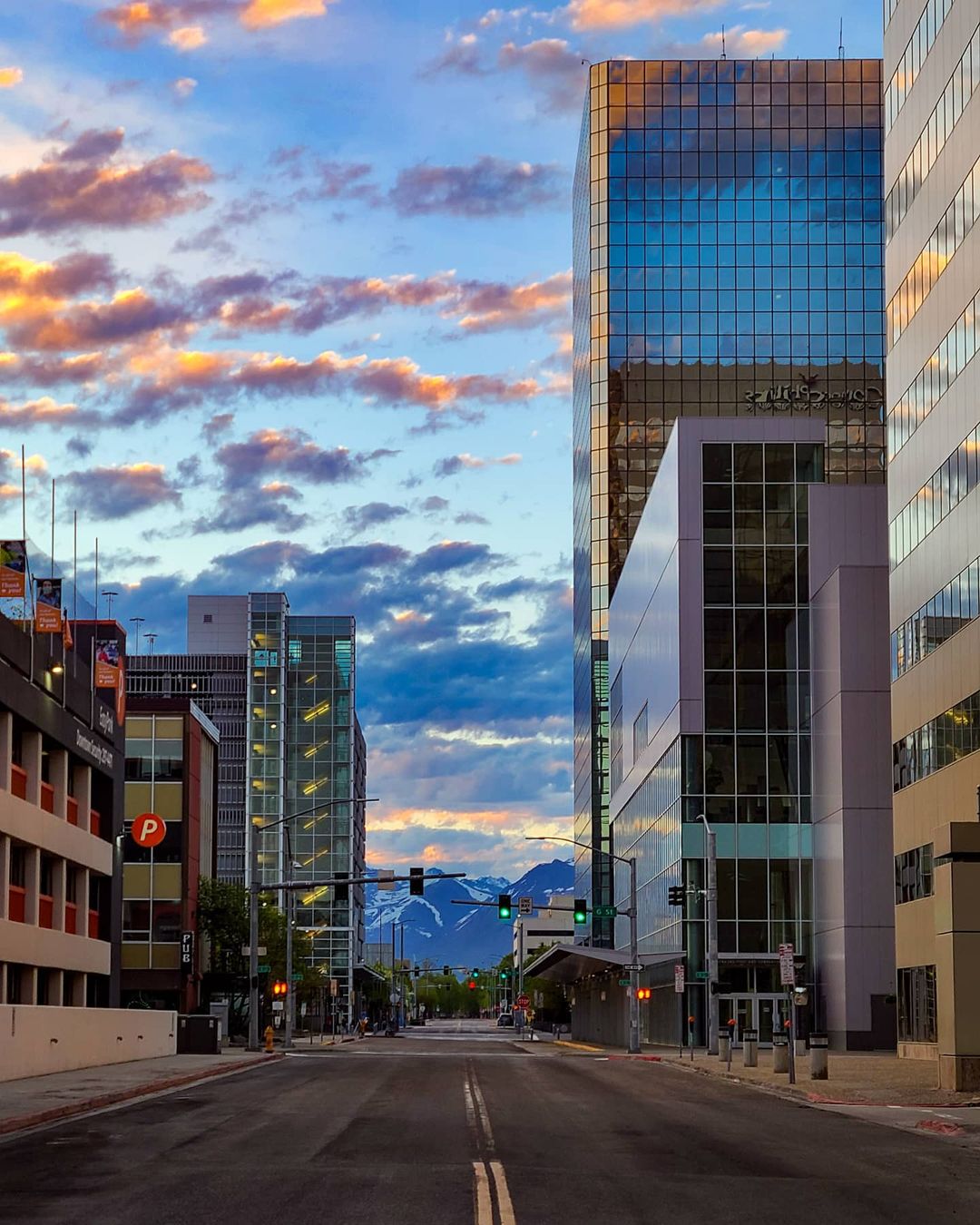 Exterior shot of Downtown Anchorage Alaska in the morning with glass buildings in foreground and clouds and snowy mountains in background | Photo by Instagram user @ rossow_photography_