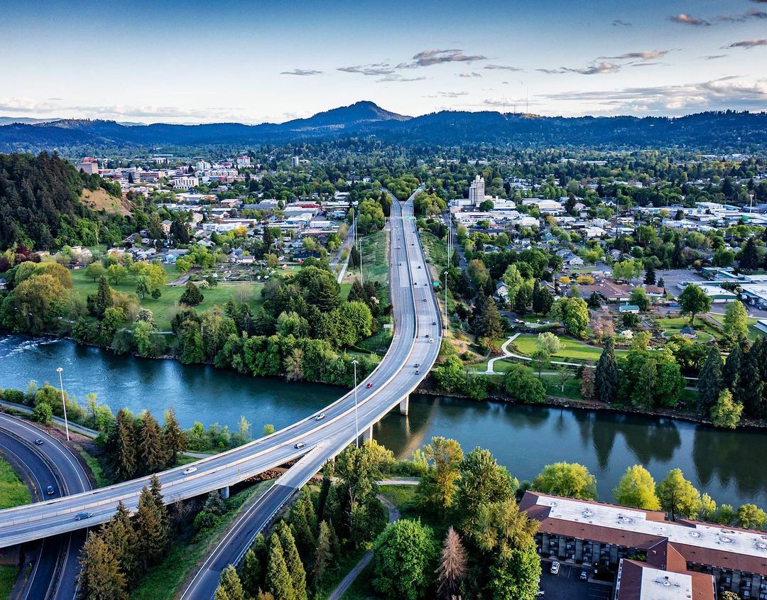 Drone shot of I-105 highway at the Willamette River in Eugene Oregon on clear day with green trees surrounding the road | Photo by Instagram user @daviesphoto