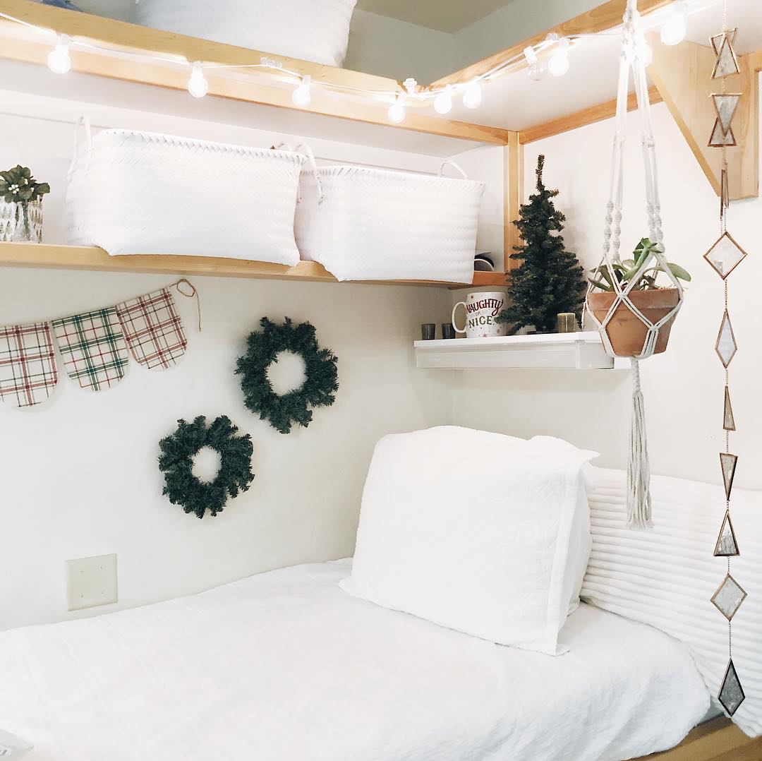 Open shelving with storage bins and decor over dorm room bed. Photo by Instagram user @emmagraceharrod
