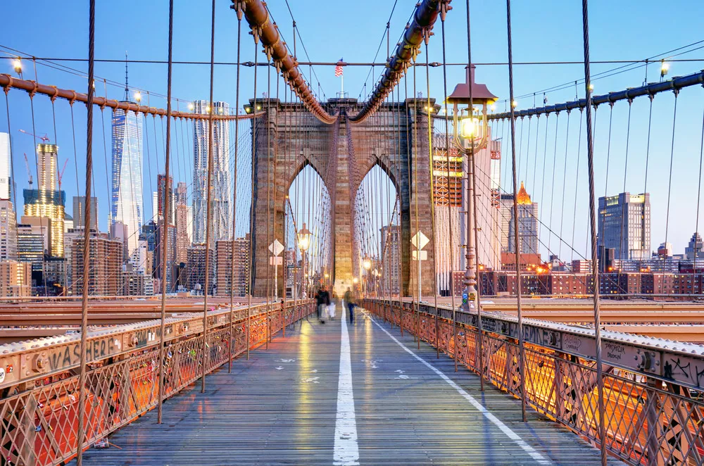 walking down the brooklyn bridge at sunset with tall buildings in the distance