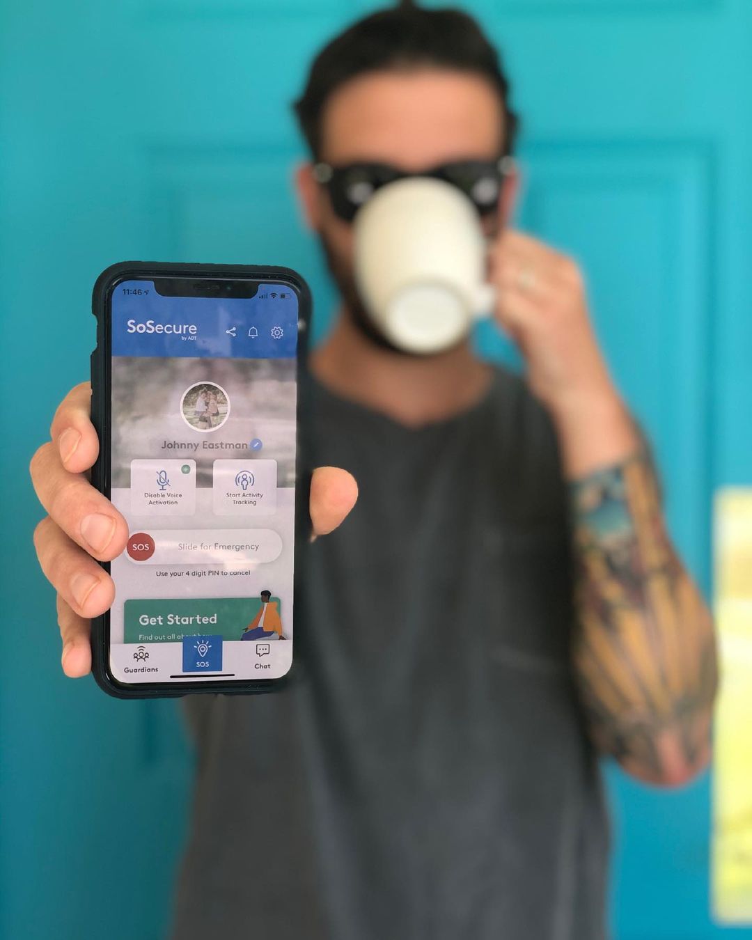 Male drinking coffee and holding up So Secure Safety App. Photo via Instagram user @thetattooedhusband