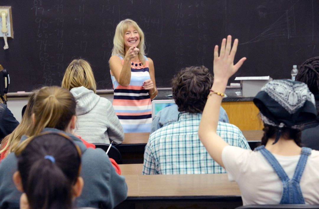 A professor at the front of a class calling on a student with her hand raised. Photo by Instagram user @fm_college