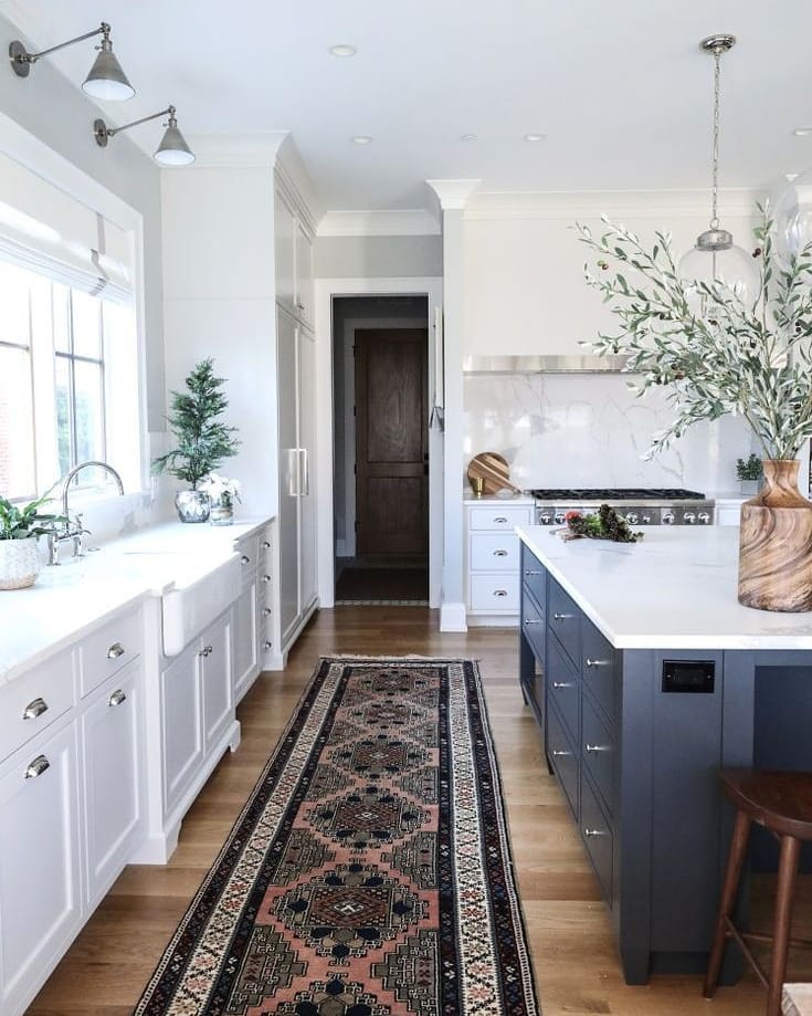 View of a kitchen with gray cabinets, marble countertops, and an enteryway rug. 