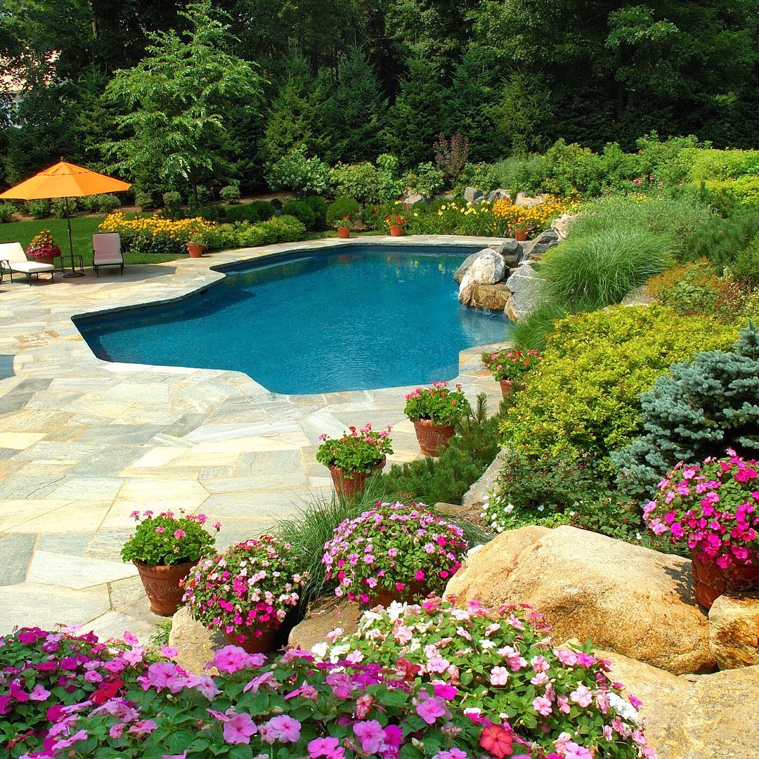 backyard pool with bright green landscape and colorful flowers. photo via @ a1hardscape