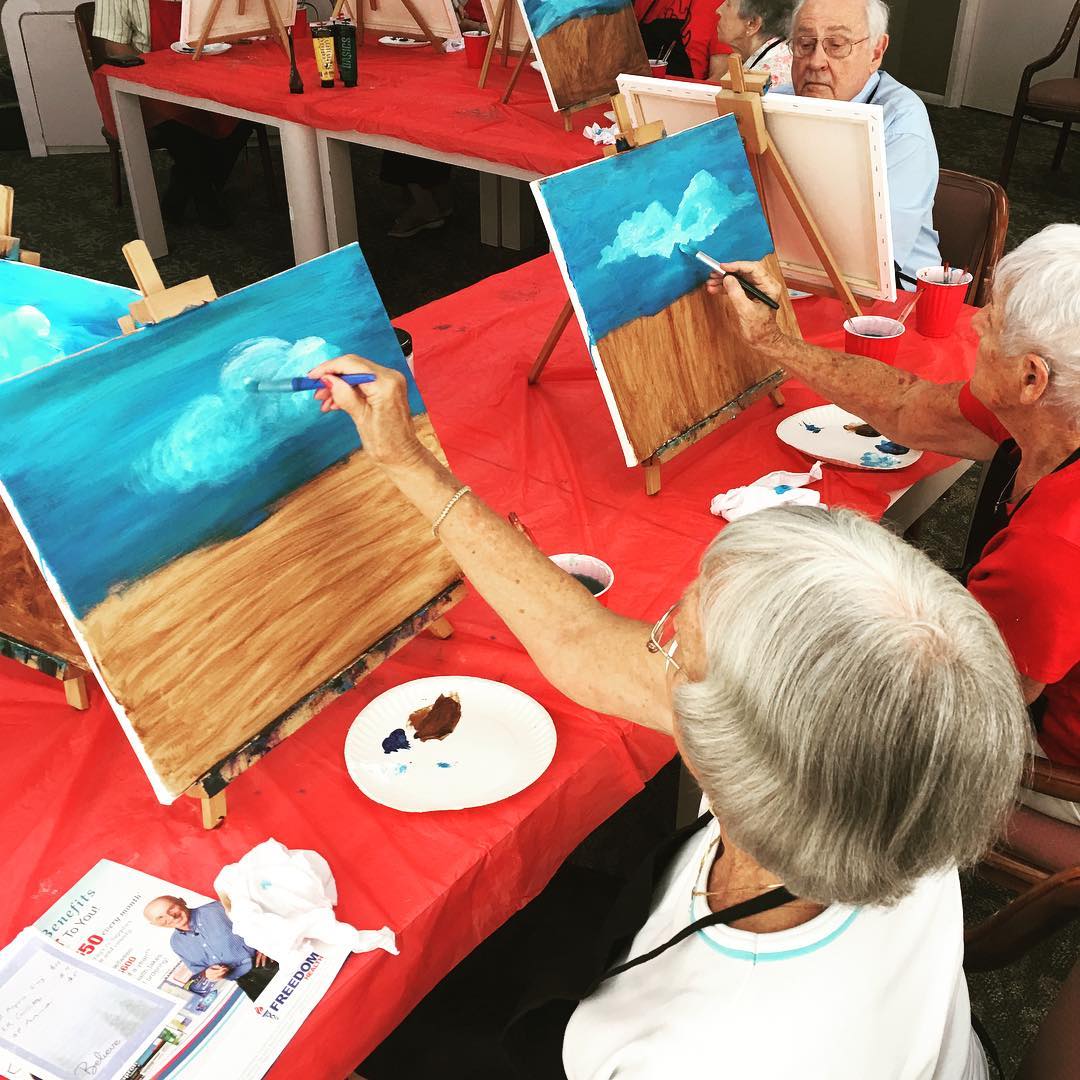 Action shot of retirees painting a landscape in a shared class. Photo by Instagram user @lakehousewestsrq.