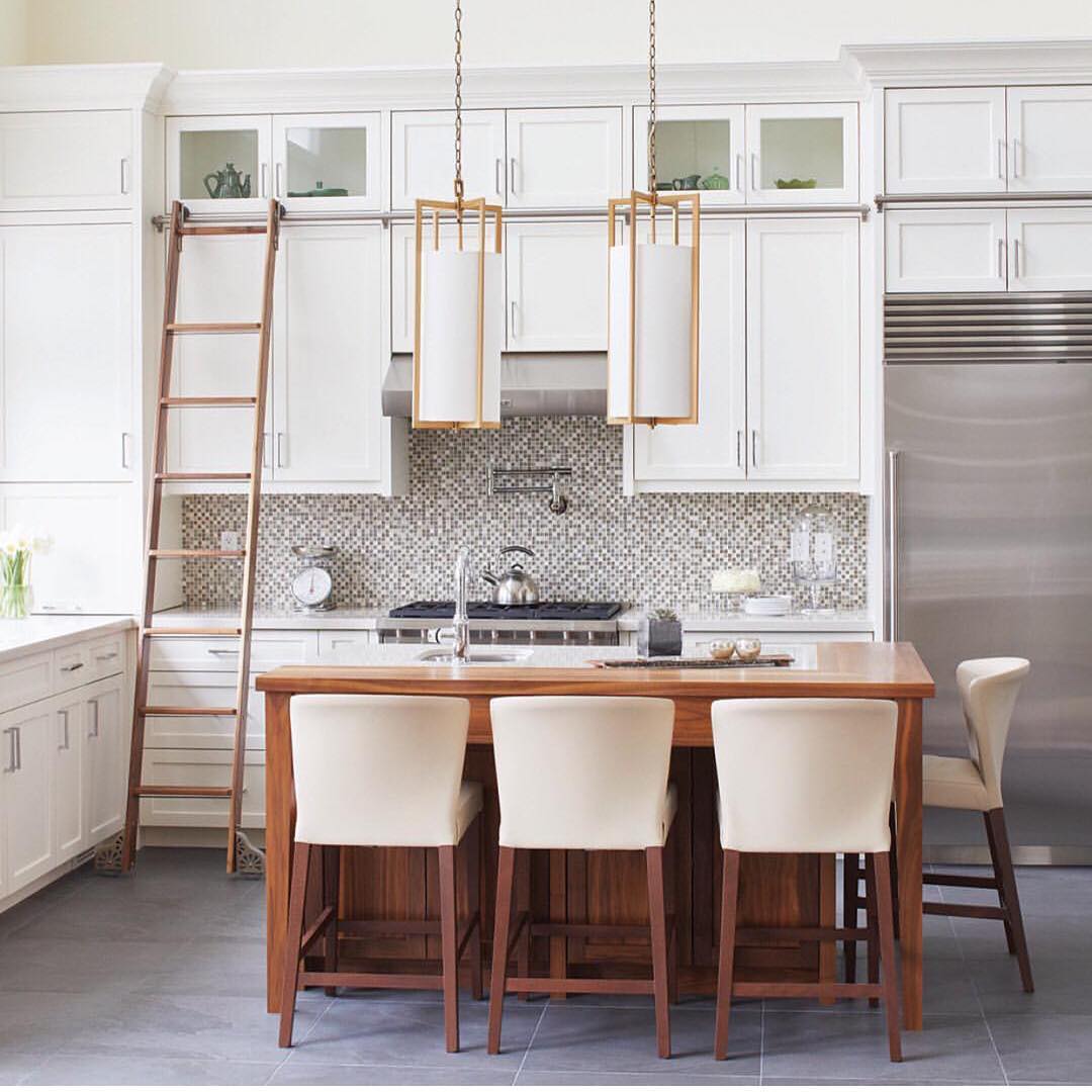A kitchen with a rolling ladder installed on the upper cabinetry is shown. Photo by Instagram username @kitchens_of_insta