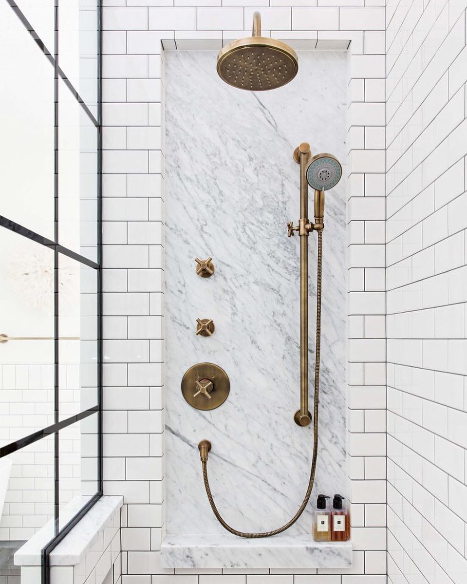 white tile shower with multiple gold shower heads photo by Instagram user @alannadunn