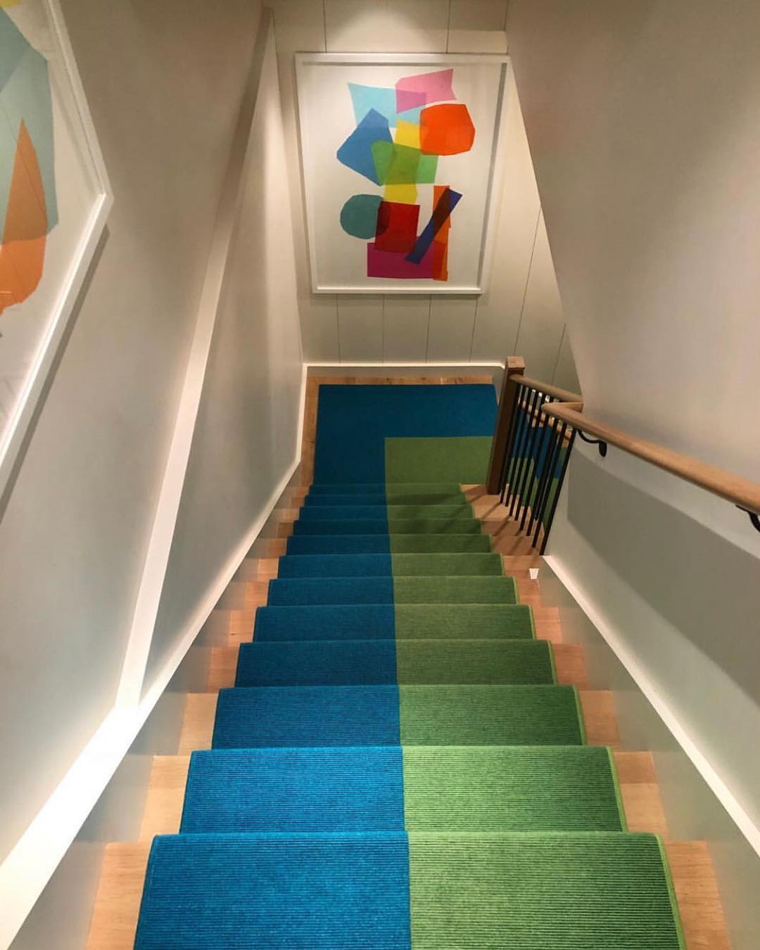 colorful basement stairwell with art on the walls and green and blue carpet photo by Instagram user @melaniemorrisinteriors