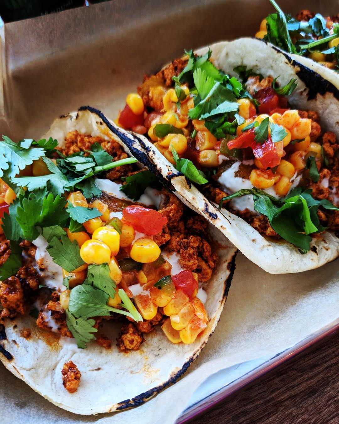 Closeup of two tacos with beef, corn, cilantro, and salsa Photo by Instagram user @screaminggoattaqueria