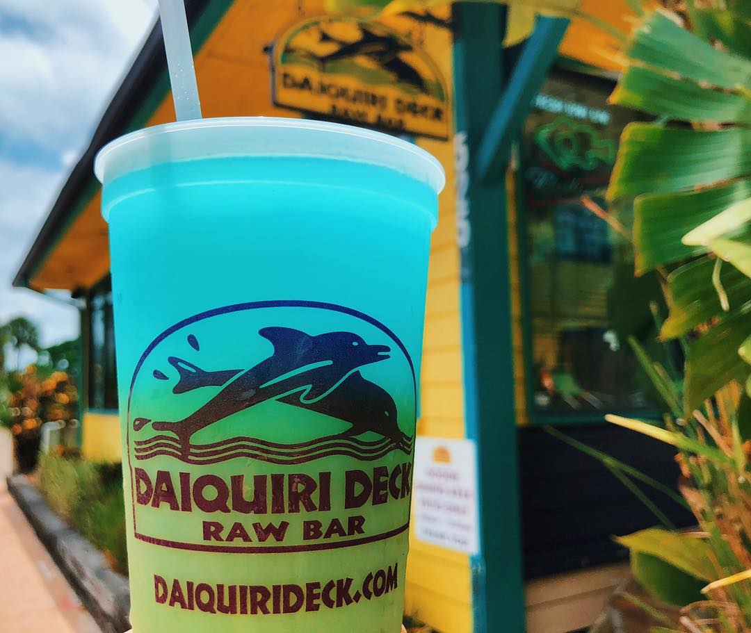 Closeup of blue and green rum drink with Daiquiri Deck Raw Bar building in background Photo by Instagram user @daiquierideck