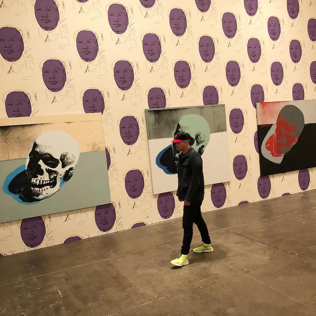 Man walks through Andy Warhol museum as 3 different paintings hang from the wall covered in wallpaper. Photo by Instagram user @johngeiger_
