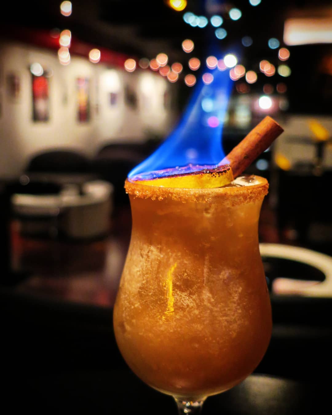 Rum drink in a hurricane glass with a cinnamon stick and piece of lemon on fire. Photo by Instagram user @mixtapepgh