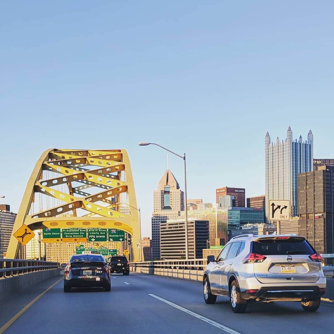 Cars drive across bridge in Pittsburgh with skyline on the right side. Photo by Instagram user @theaaronm