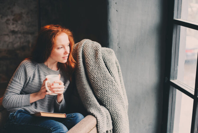Red haired minimalist woman sitting and looking out window.