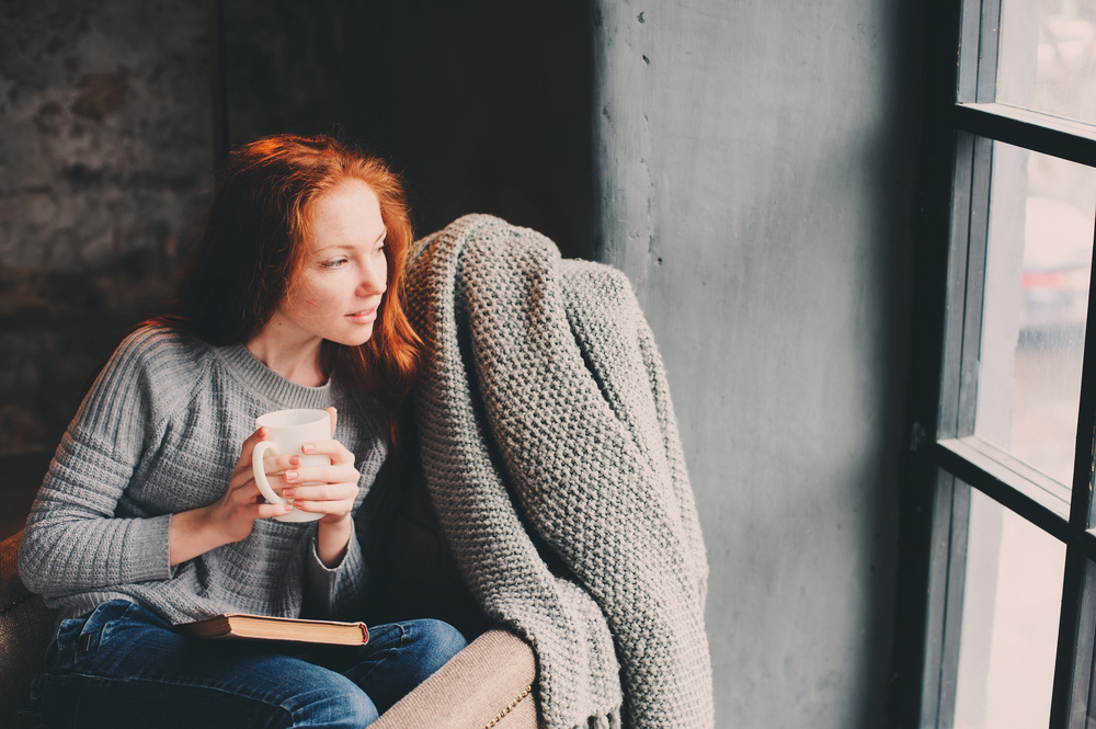 Red haired minimalist woman sitting and looking out window.