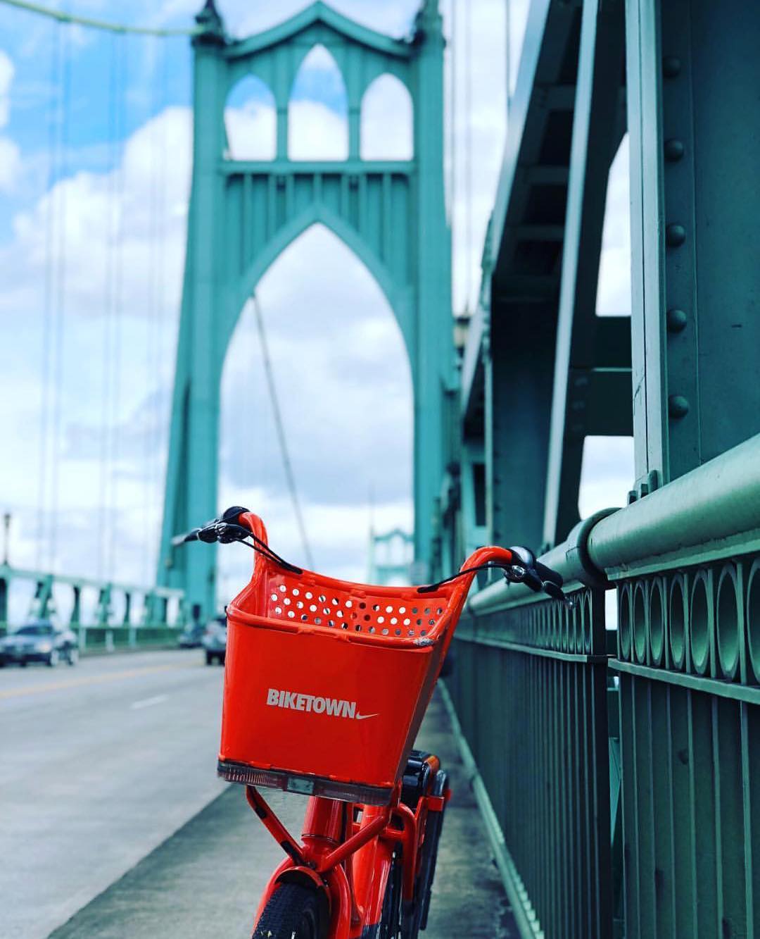 Orange Biketown bike resting against bridge railing with cars driving in the background Photo by Instagram user @portland