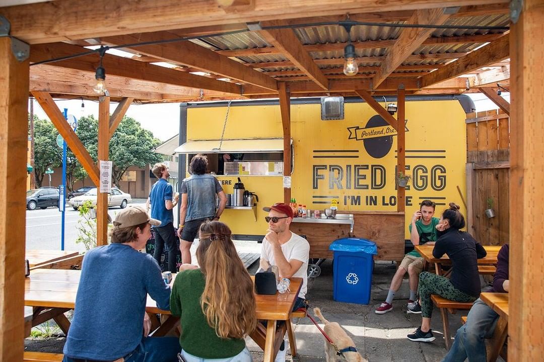 Diners seated at picnic tables under a shelter near a food truck Photo by Instagram user @friedegglove