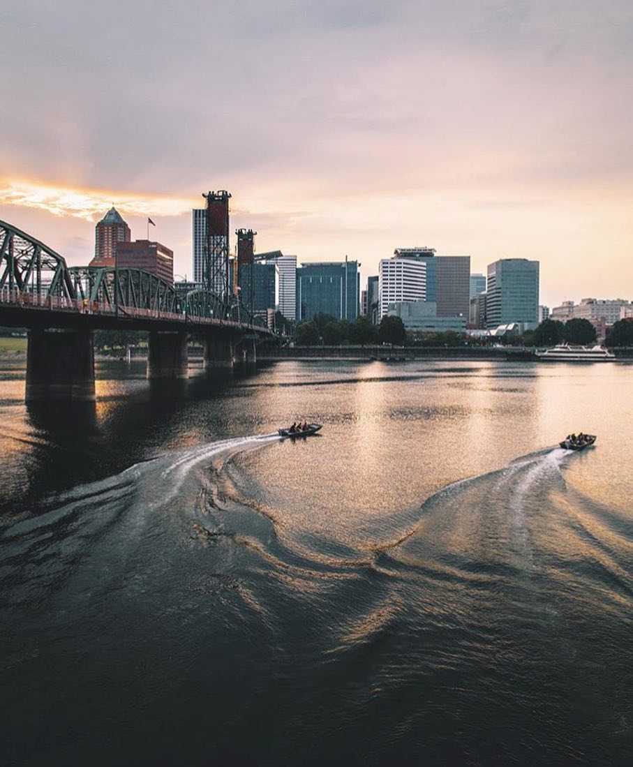 View of Willamette River with two boats in the water and Portland skyline in the background Photo by Instagram user @portland