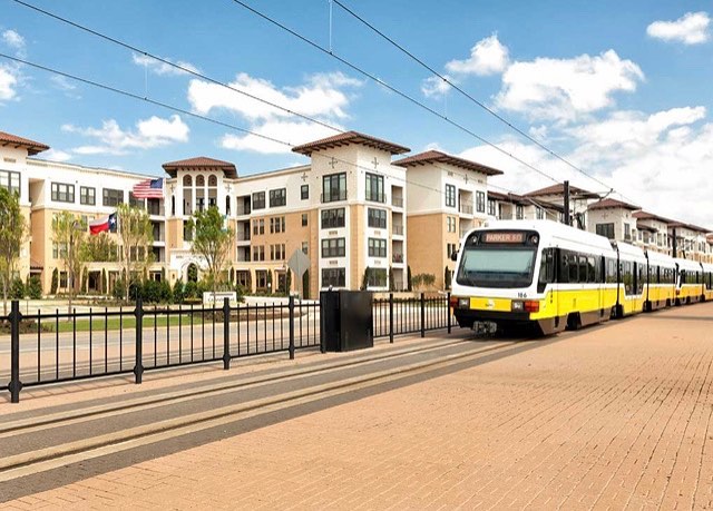A yellow tram speeds past a beige street and buildings on a sunny day. Photo via Instagram user @amlicampiontrail