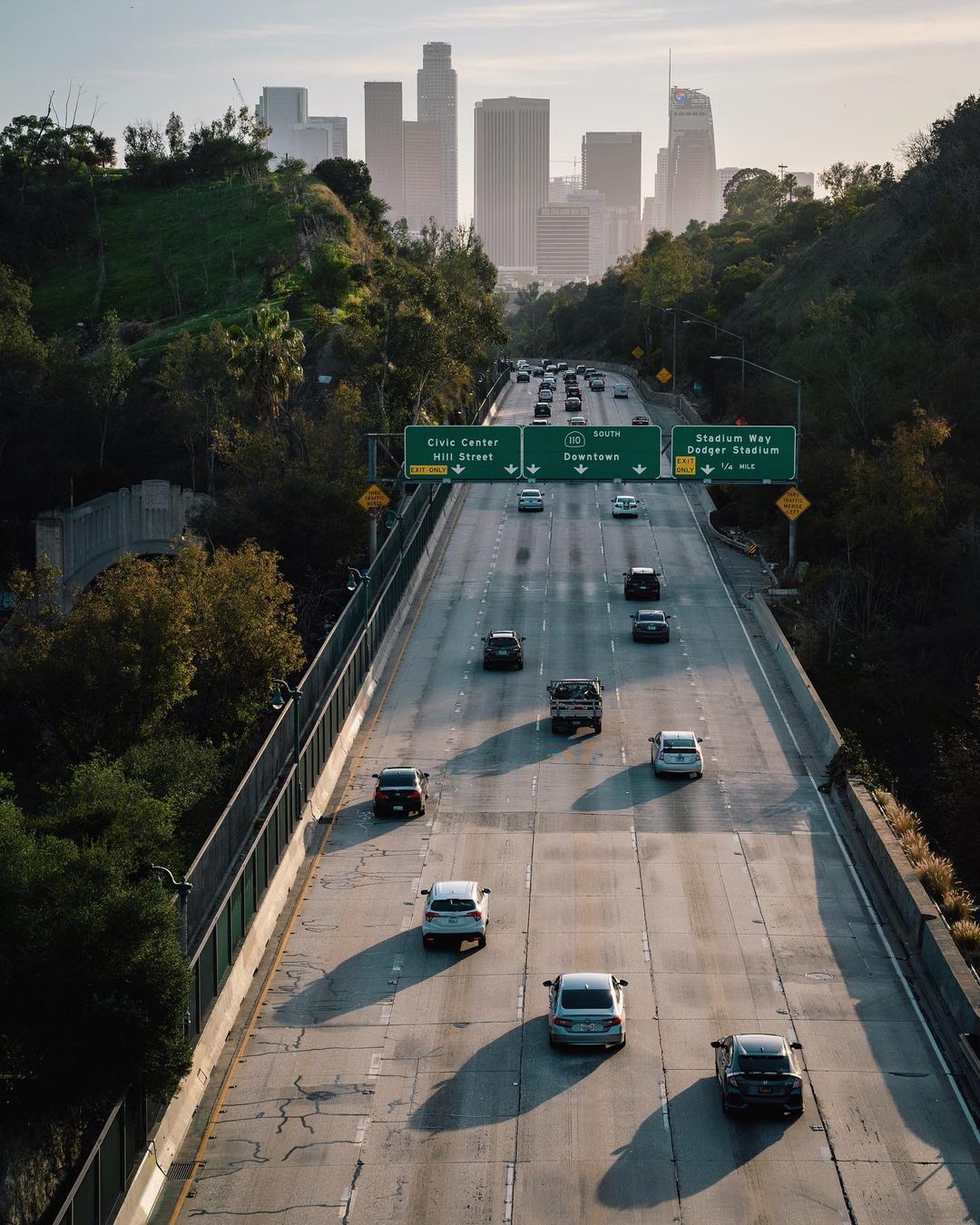 Los Angeles highway surrounded by green trees and Downtown buildings in distance. Photo by Instagram user @eforth