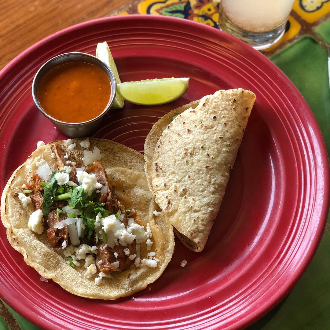 Two tacos with lime and salsa on a red plate Photo by Instagram user @elranchito214