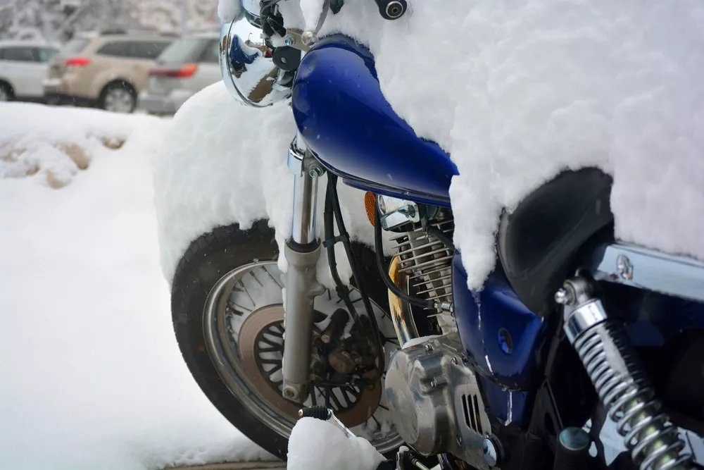 Blue motorcycle in Winter with snow piled on top.