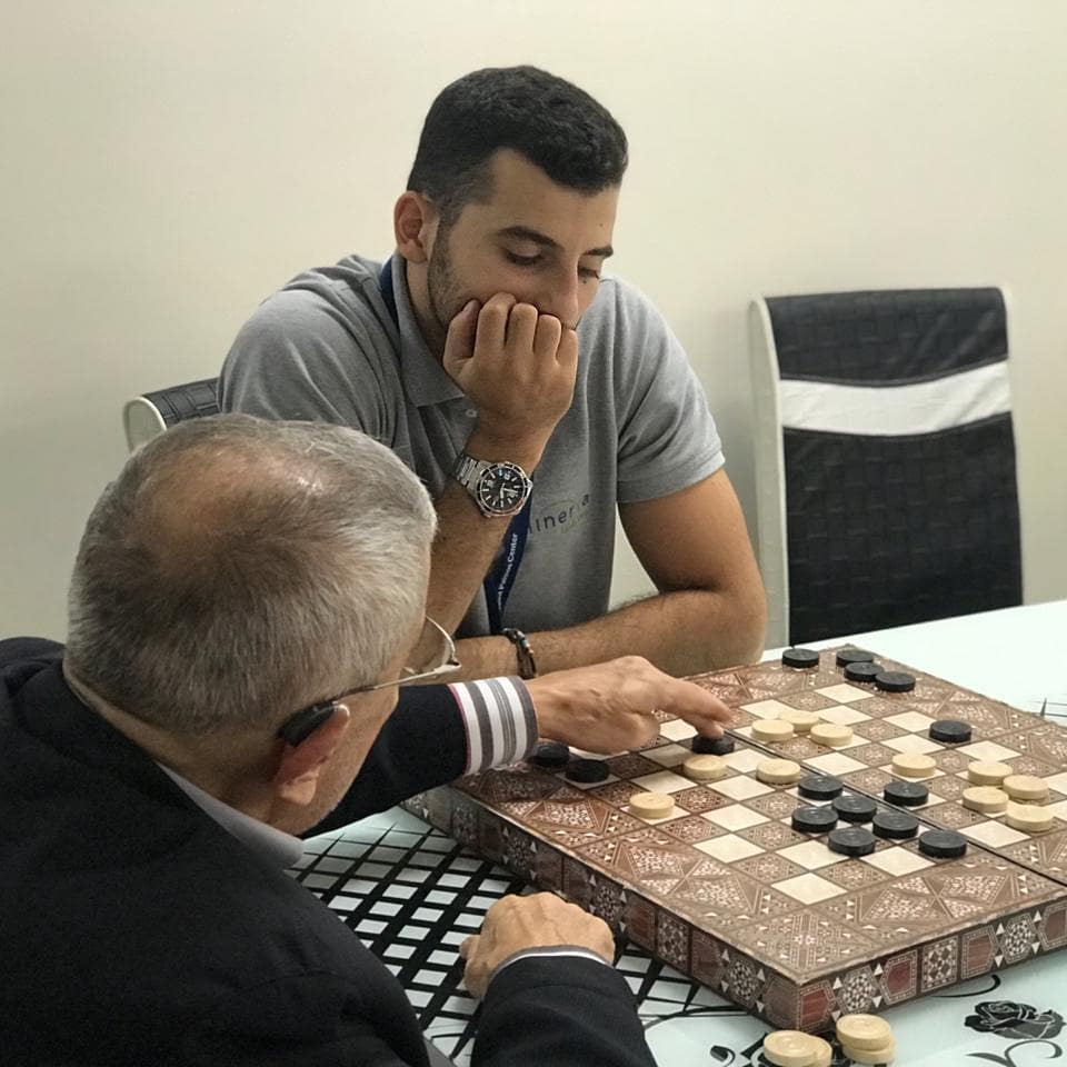 Elderly Man Playing Checkers with Young Man. Photo by Instagram user @minervaadultcare