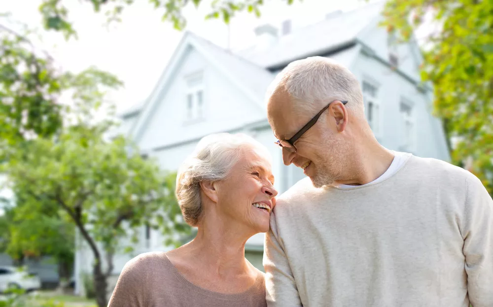 Retired white woman and man standing outside home.