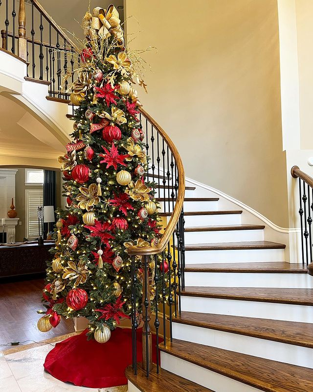 Photo of a Christmas tree wrapped around a winding staircase with large ornaments. Photo by instagram user @brittany.daniellesmd