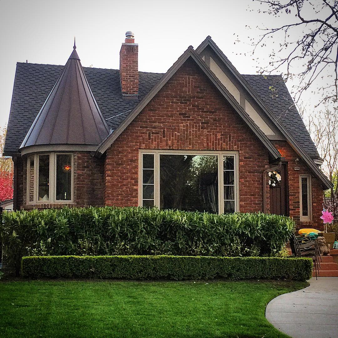 Front of single-family brick home with a spire and large picture window in front. Photo by Instagram user @lovelyoldhomes