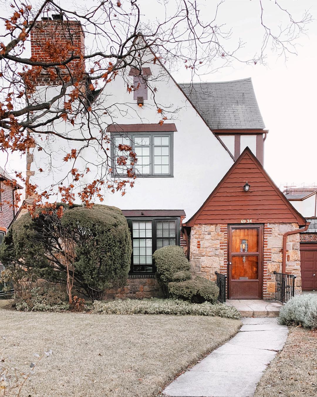 Quaint cottage style white colored home with traditional red stone and siding. Photo by Instagram user @nycforesthills