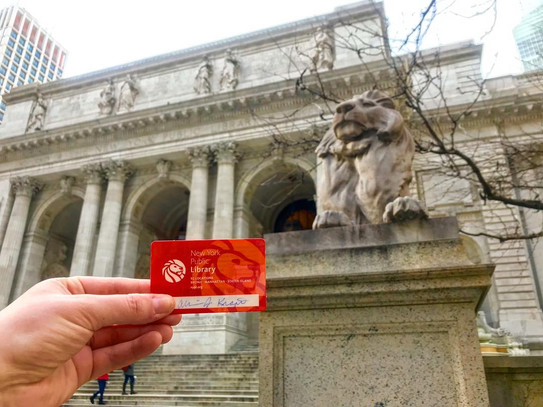 Person Holding Up Library Card in Front of the New York Public Library. Photo by Instagram user @ajkrafty