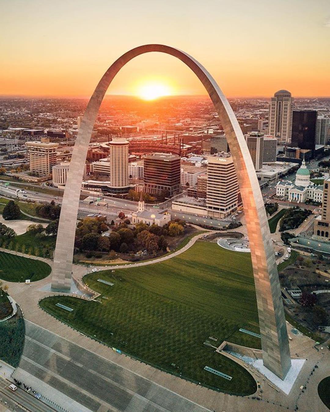 An aerial view of the St. Louis Gateway Arch with the sunset in the distance. Photo by Instagram user @explorestlouis