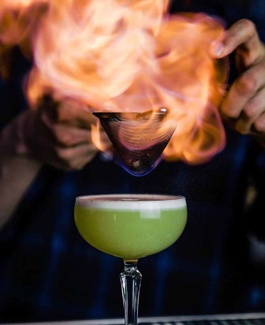 A bartender serves a green martini with fire on top. Photo by Instagram user @truststl