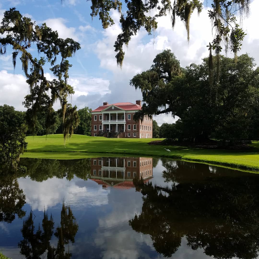 Large college building in the background with a clear pond and trees in the foreground. Photo by Instagram user @draytonhall