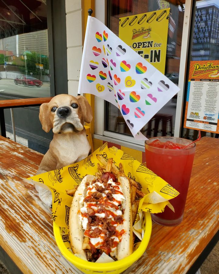 One of Dirty Frank's Queen Nina dogs displayed in front of a dog statue holding a LGBTQ pride flag. Photo by Instagram user @dirtyfranksdogs